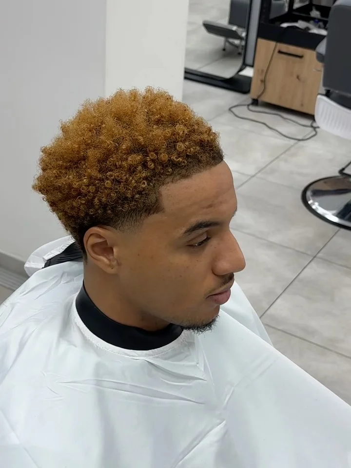 Client with dyed-blonde textured curls and a clean skin fade at ELEMENT Barbershop